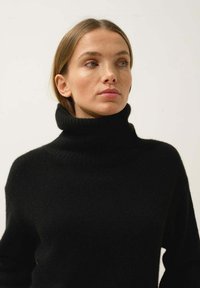 Mustat korkeakauluksinen neule, joka on valmistettu pehmeästä materiaalista. Siinä on ribbireunus ja rento istuvuus, pitkät hihat sekä sileä pinta.