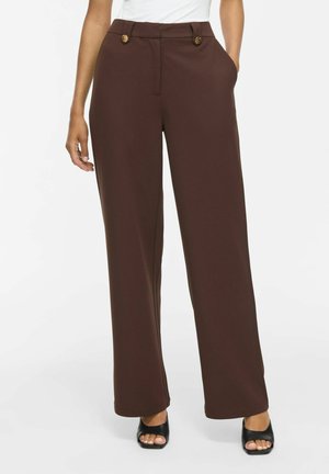 Pantalon marron à jambes larges avec des boutons à la taille, porté avec des sandales à talons noires à bout ouvert et un haut blanc.