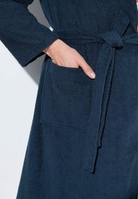 Navyblå frottébadrock med bälte och en framficka, i en texturerad finish och med vida ärmar.