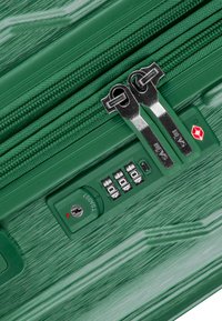 Valigia rigida verde con finitura testurizzata, dotata di doppie cerniere, una combinazione di lucchetto e un foro chiave approvato dalla TSA.