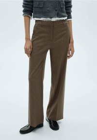Pantalons à carreaux marron avec une coupe ajustée, présentant une texture lisse et un design à jambe droite. Comprend des poches avant et une fermeture éclair.