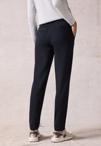 Marineblauwe slim-fit broek van geweven stof, met een soepele textuur, twee achterzakken en gecombineerd met witte en beige sneakers.