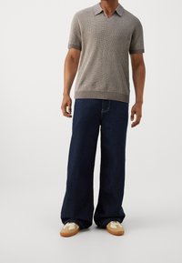 Szary dzianinowy polo z krótkim rękawem i dekoltem w serek, w połączeniu z ciemnoniebieskimi dżinsami o szerokich nogawkach oraz beżowymi sneakersami z białymi akcentami.