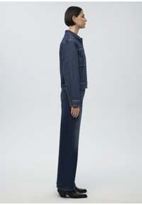 Denim jacket and high-waisted jeans in dark blue. The jacket has a classic design with front pockets and buttons, paired with heeled boots.