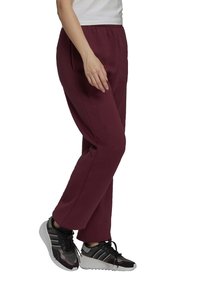 Maronfärgade sweatpants med elastisk midja, rak ben-design och en slät textur, kombinerat med svarta träningsskor med vita sulor.