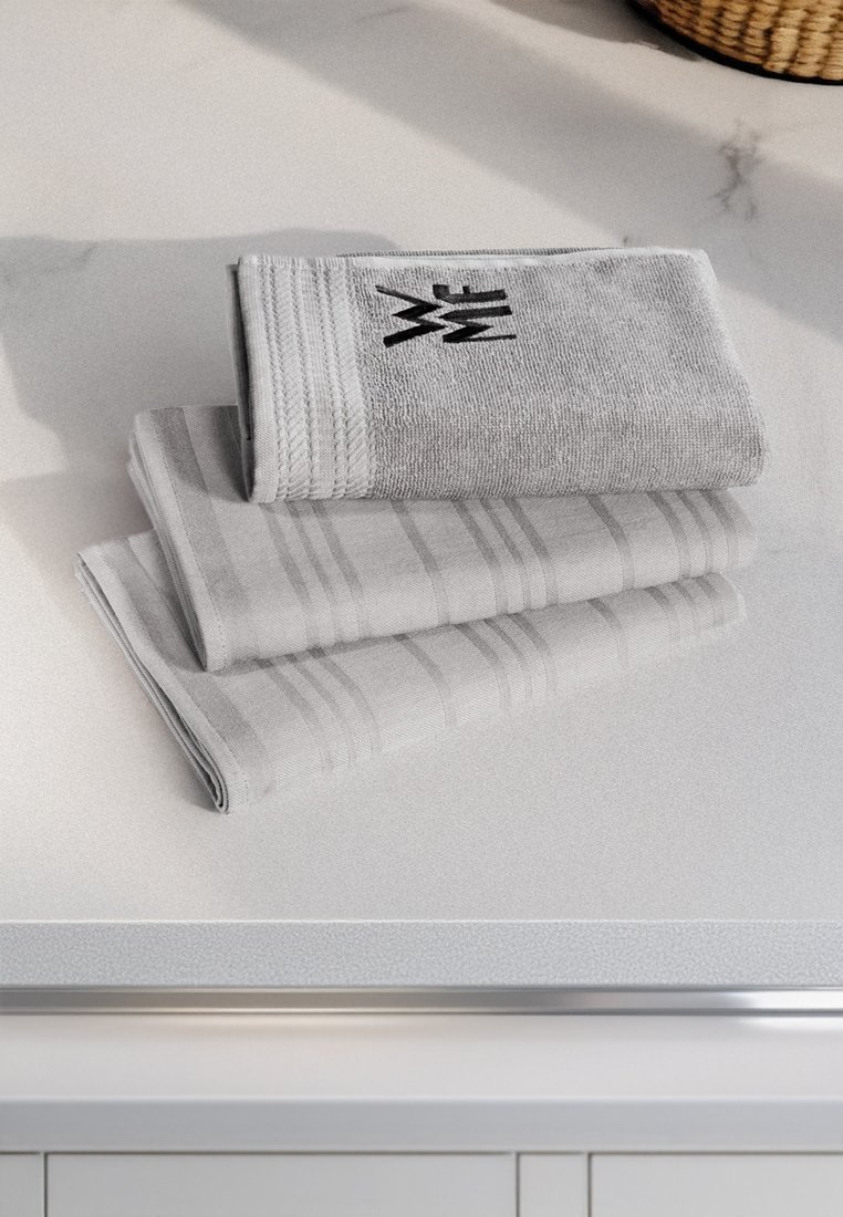 Grau gestreifte Handtücher auf einer Arbeitsplatte gestapelt. Das oberste Handtuch zeigt ein strukturiertes Streifenmuster und ein schwarzes Logo. Die unteren Handtücher weisen dezente Streifenmuster auf.