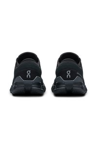 Baskets de sport noires avec une tige en maille, semelle rembourrée et motif de crampons prononcé. Les caractéristiques comprennent un logo blanc sur le talon.