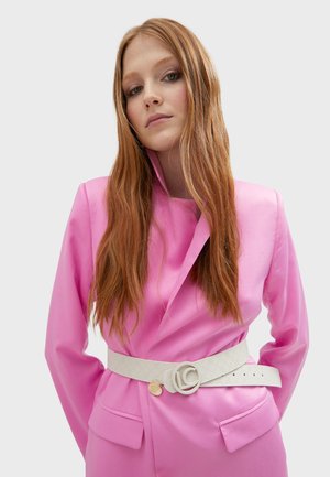 Blazer entallado rosa con solapa, combinado con un cinturón blanco texturizado que presenta una hebilla circular y un detalle de logo.