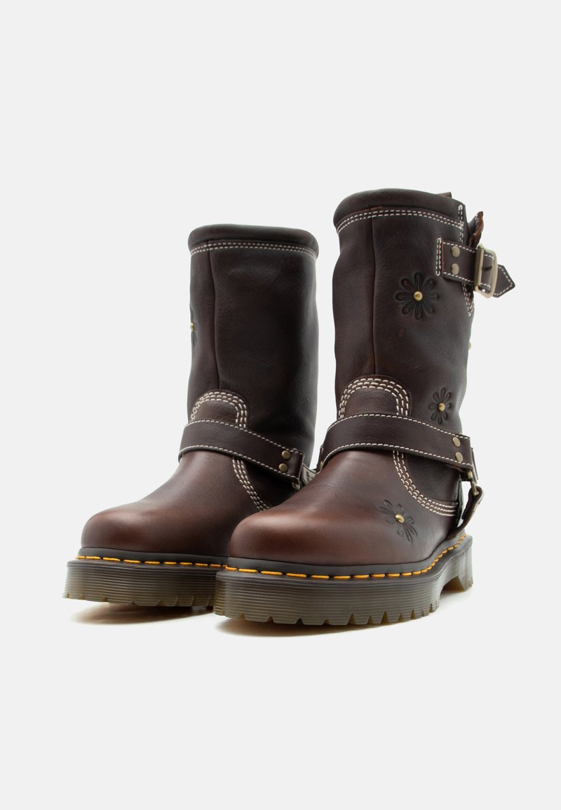 Dunkelbraune Lederstiefel bis zur Mitte der Wade mit floraler Prägung, doppelten Riemen mit Metall-Schnallen, dicke Gummisohlen mit gelber Naht, auf weißem Hintergrund.