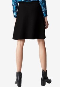 Gonna nera a linea A con una texture liscia, dotata di una vita. Indossata con stivaletti neri con tacco alla caviglia. Top blu a fantasia sopra.