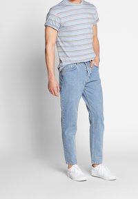 Jasnoniebieska koszulka w paski z podwiniętymi rękawami, zestawiona z jasnoniebieskimi dżinsami i białymi sneakersami. Codzienny strój, luźny krój.