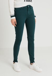 Jeans skinny verde oscuro hechos de una mezcla de algodón, con un diseño clásico de cinco bolsillos y combinados con zapatillas blancas.