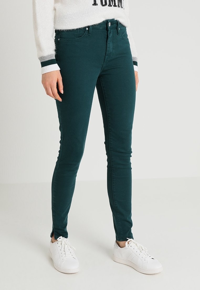 Jeans skinny verde oscuro hechos de una mezcla de algodón, con un diseño clásico de cinco bolsillos y combinados con zapatillas blancas.