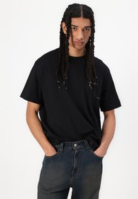 Sort bomulds T-shirt med afslappet pasform, rund halsudskæring og korte ærmer, parret med højtaljede mørke denim jeans.