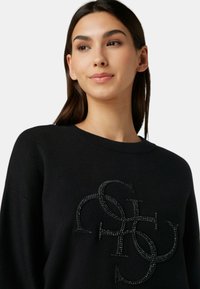 Maglione nero con un design testurizzato e preziosi dettagli neri stratificati che formano lettere decorative. Collo rotondo e maniche lunghe.