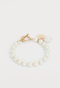 Pulsera de perlas blancas con cierre de toggle en tono dorado y charm, que presenta una textura suave y brillante, junto con un acento de perla de forma irregular.