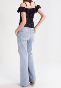 Top de encaje azul marino con volantes descubiertos en los hombros, combinado con jeans de pierna recta azul claro que tienen bolsillos traseros y un ajuste relajado.