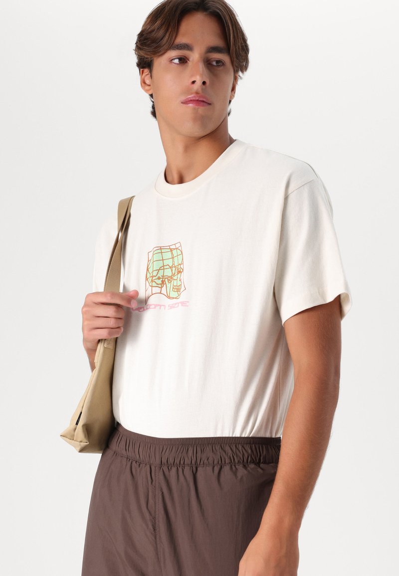 Light beige cotton t-shirt with short sleeves, featuring a graphic design in green and orange. Paired with elastic brown shorts.