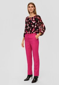 Zwarte blouse met kleurrijke abstracte patronen, gecombineerd met strakke roze broek. Model draagt zwarte hakken tot de enkel.