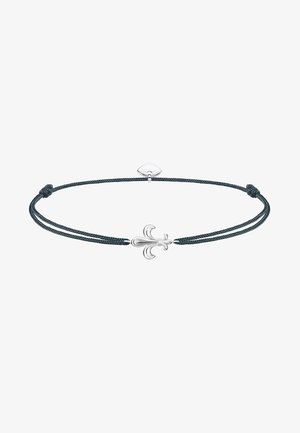 Bracelet cordon noir ajustable avec un charm fleur-de-lis en argent centré et un petit cœur en argent près du fermoir.