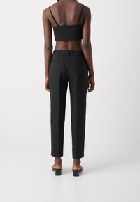 Schwarze, maßgeschneiderte Hosen mit geradem Bein, glatter Stoff und zwei Gesäßtaschen, kombiniert mit einem schwarzen Cropped Top und schwarzen Absätzen.