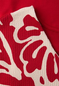 Gros plan sur un tissu texturé rouge et blanc avec des motifs floraux abstraits audacieux sur un fond de tissu rouge uni.