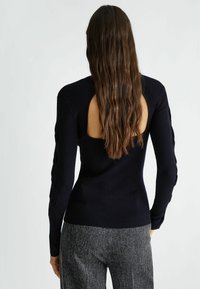 Maglione a coste blu navy con maniche lunghe e schiena scoperta. Presenta maniche testurizzate con un design intrecciato e una silhouette aderente. Abbinato a pantaloni grigi testurizzati.