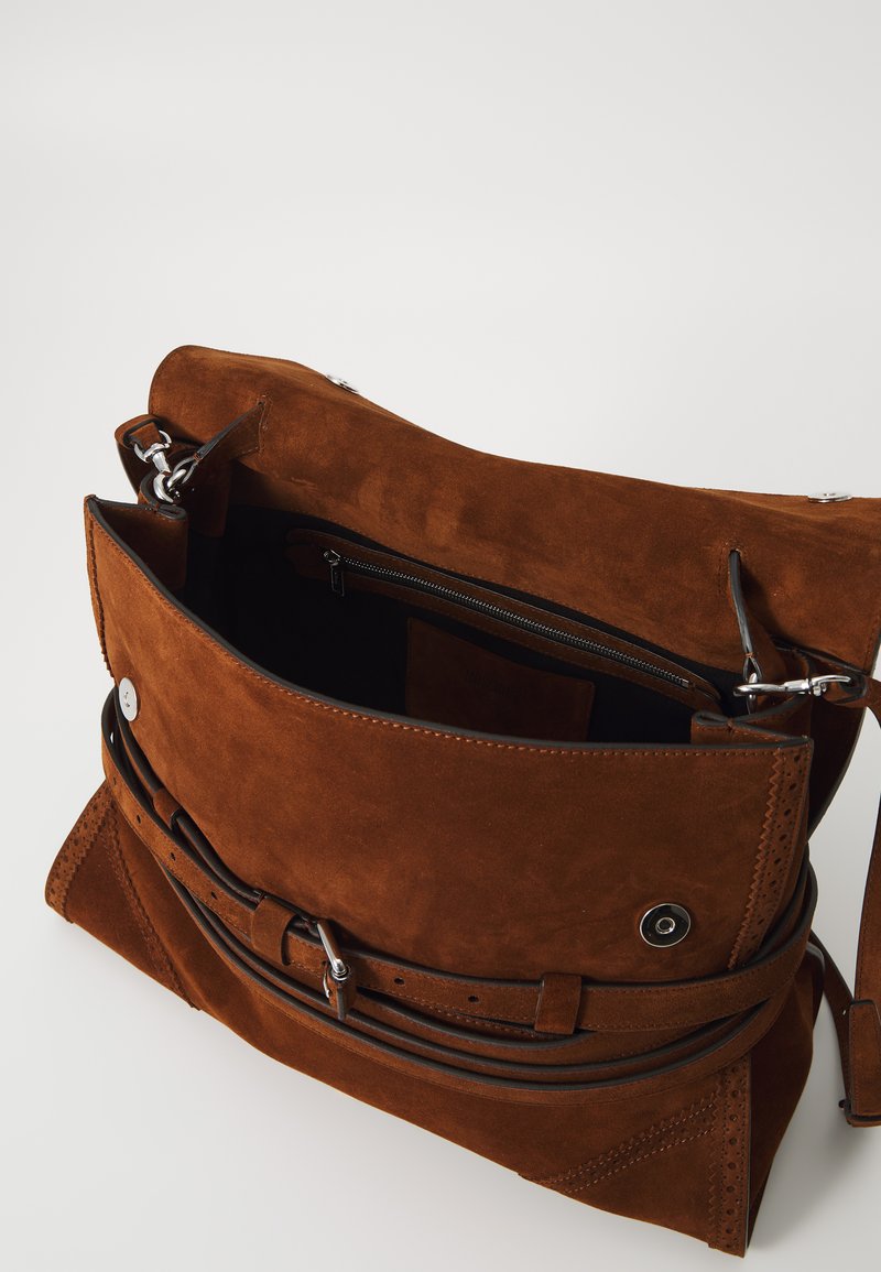 Brun mockaskinn-väska med en strukturerad design, som har en dragkedja ficka, justerbar läderrem och dekorativa sömnadsdetaljer.