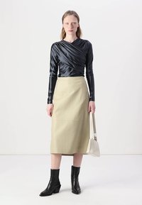 Svart satin langermet topp med vridd frontdesign, paret med en lys brun skinnskjørt til kneet og svarte ankelstøvletter med hæl.