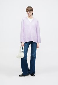 Izredno velik vijoličen pulover z v-izrezom, kombiniran z modrimi razširjenimi kavbojkami in majhno belo torbico. Črni ravni čevlji dopolnijo videz.