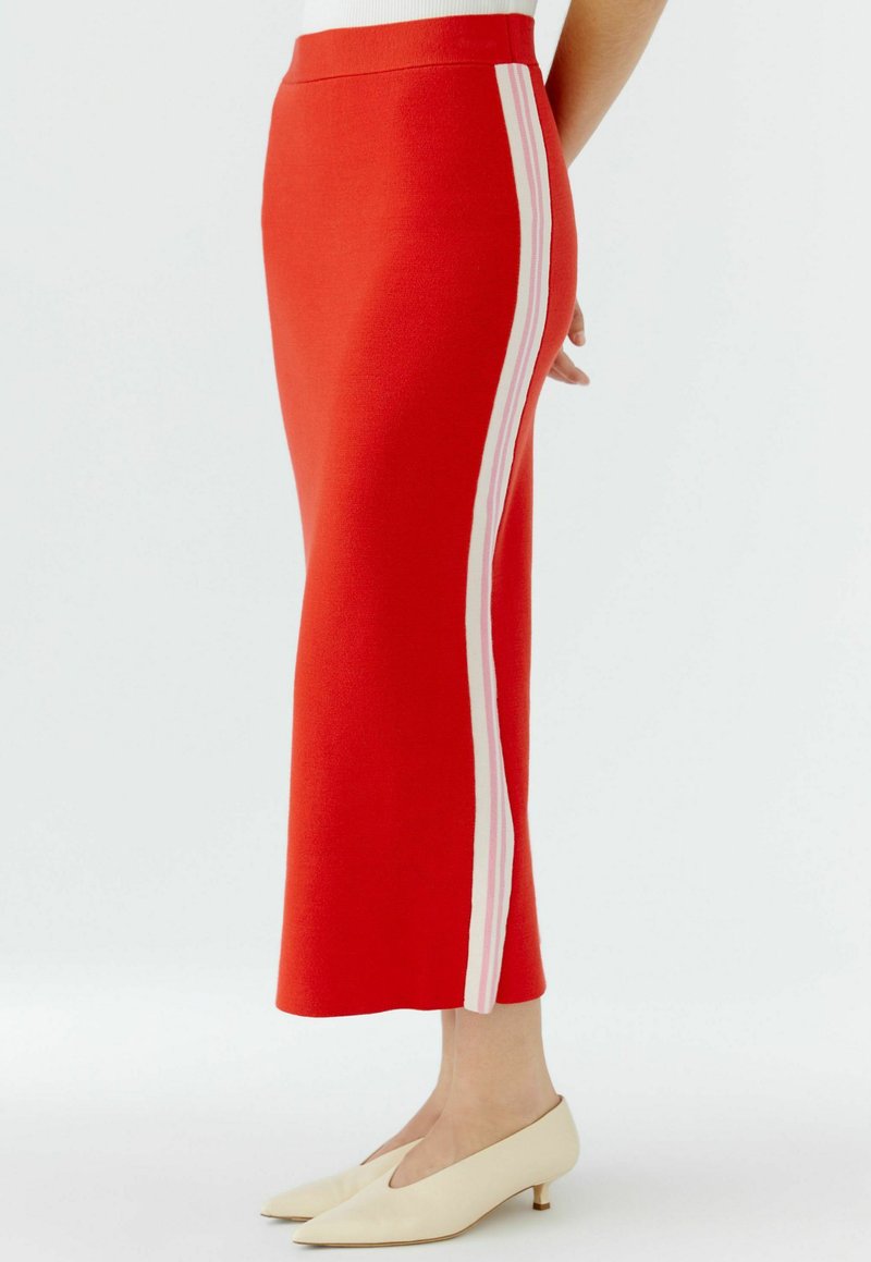 Jupe midi rouge tricotée avec des rayures blanches latérales, dotée d'une taille ajustée et d'une texture lisse. Associée à des talons slip-on couleur crème.