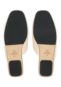 Paire de chaussures en cuir couleur crème vues par les semelles, avec des embouts de talons carrés noirs et des marquages de taille 37.