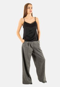 Camisole nera in satin con bordi in pizzo abbinata a pantaloni a gamba larga grigi a quadri. I pantaloni hanno una vestibilità ampia e tasche laterali.