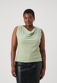 Top sin mangas de color verde claro con un escote drapeado, tejido texturizado y diseño ajustado, combinado con una falda de cuero negra.