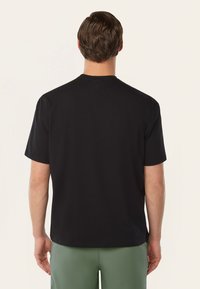 Zwarte korte mouwen t-shirt van katoen, met een ronde hals en een klein logodetail op de achterkant, gecombineerd met groene shorts.