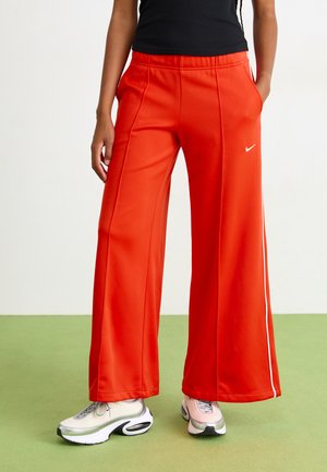 Røde vide bukser laget av glatt stoff, med sidelommer og hvit piping. Nike-logo plassert på venstre hofte.