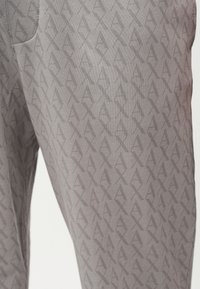 Γκρι παντελόνι με ένα διακριτικό επαναλαμβανόμενο μοτίβο από αλληλεπικαλυπτόμενα γράμματα "A" και "X" σε λίγο πιο σκούρα απόχρωση.