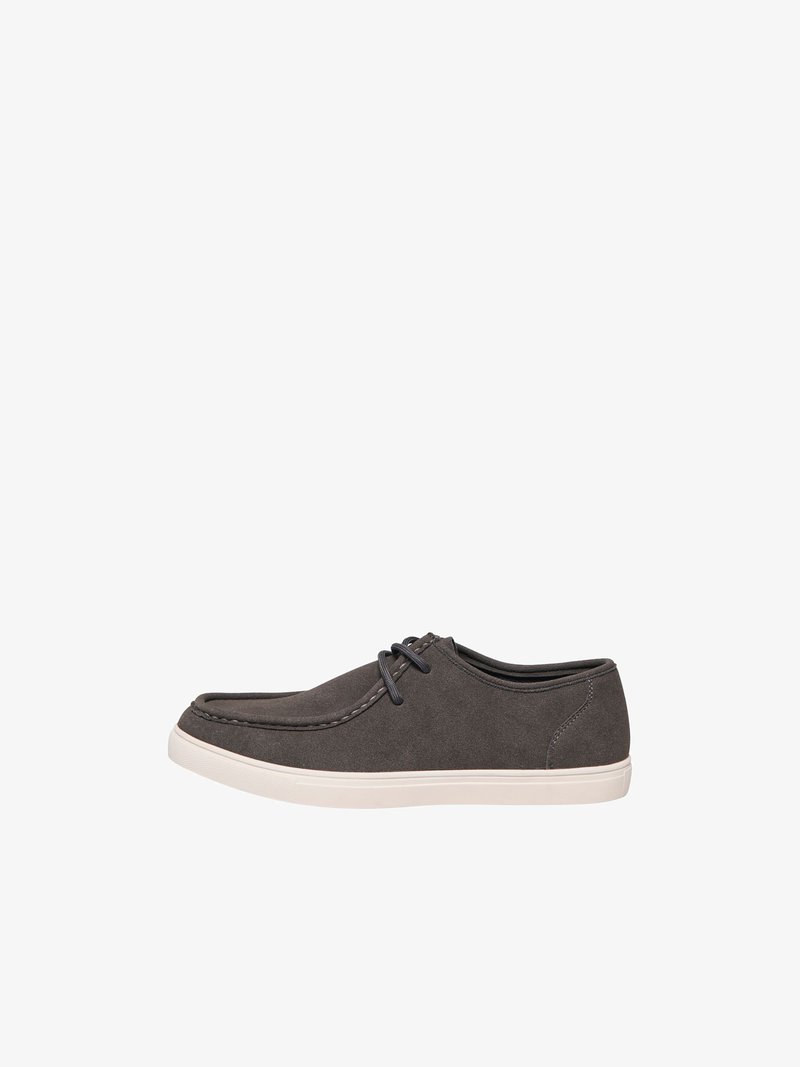 Chaussure décontractée en daim gris foncé à lacets avec semelle en caoutchouc blanche, vue de côté sur fond blanc.