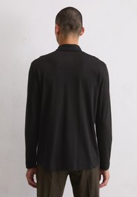 Zwarte longsleeve shirt met een zachte textuur en een klassieke kraag. Heeft een rechte zoom en een minimalistisch ontwerp, gedragen met olijfgroene broek.
