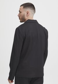 Black tailored blazer with a notched collar, single-button closure, and smooth texture, featuring a clean back design and fitted sleeves.