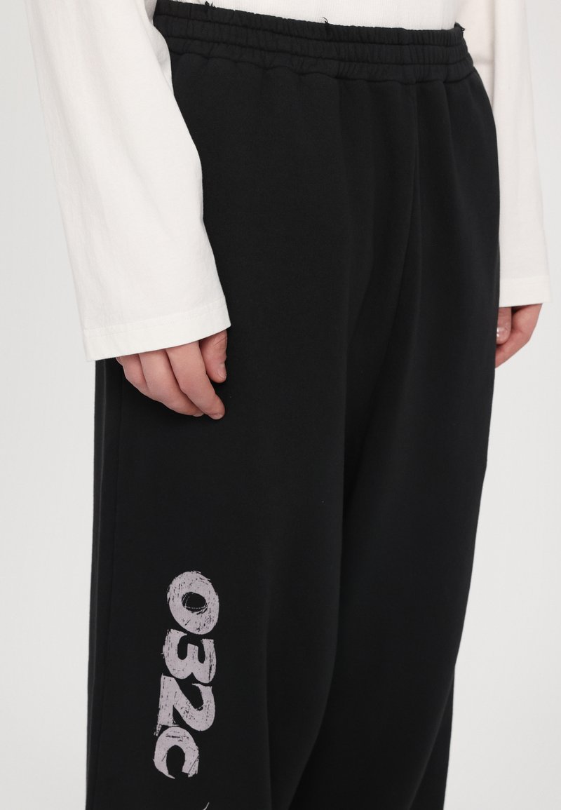Schwarze Jogginghose mit strukturiertem Finish, ausgestattet mit einem elastischen Bund und einem weißen Grafikdruck "032C" auf dem linken Bein.