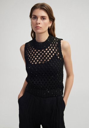 Black knitted sleeveless top with a honeycomb pattern, ribbed neckline, and subtle sequins. Worn with textured black high-waisted pants.