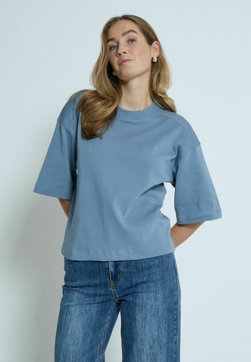 Kortærmet, kort t-shirt i blødt blå bomuld med rund halsudskæring og afslappet pasform. Kombinationen med høj talje jeans.