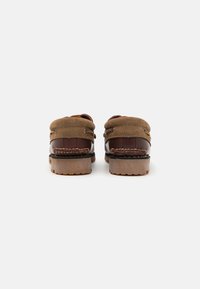 Mocassins en cuir marron avec des accents textiles, présentant une finition lisse, une forme arrondie et une semelle en caoutchouc durable. Détails en double couture au niveau du talon.