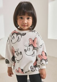 Sweatshirt blanc avec des impressions répétées de Minnie Mouse noires et roses, col rond, et poignets et ourlet côtelés, associé à des leggings noirs.
