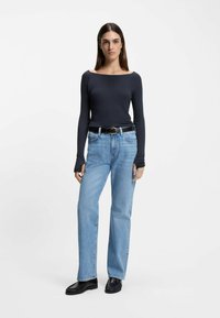Ciemny dopasowany top z długim rękawem i dekoltem odsłaniającym ramiona, w połączeniu z jasnoniebieskimi jeansami o prostych nogawkach i czarnymi wsuwanymi butami.