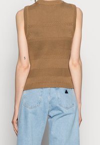 Un top sans manches en tricot marron présente des rayures horizontales et un ourlet côtelé, associé à un jean taille haute bleu clair et un détail en forme de triangle.