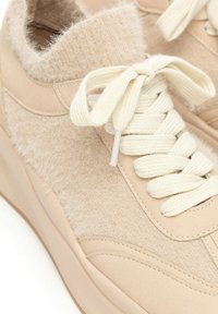 Scarpe sportive beige con una tomaia in pelle liscia e un inserto in tessuto morbido. Design con lacci e dettagli testurizzati sul lato.