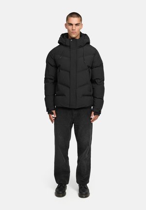 Giacca a vento nera con design trapuntato, chiusura con zip e cappuccio regolabile. Abbinata a pantaloni scuri e stivaletti neri con lacci.