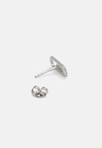 Pendiente de plata con forma circular y un borde texturizado intrincado, acompañado de un cierre decorativo en forma de mariposa.
